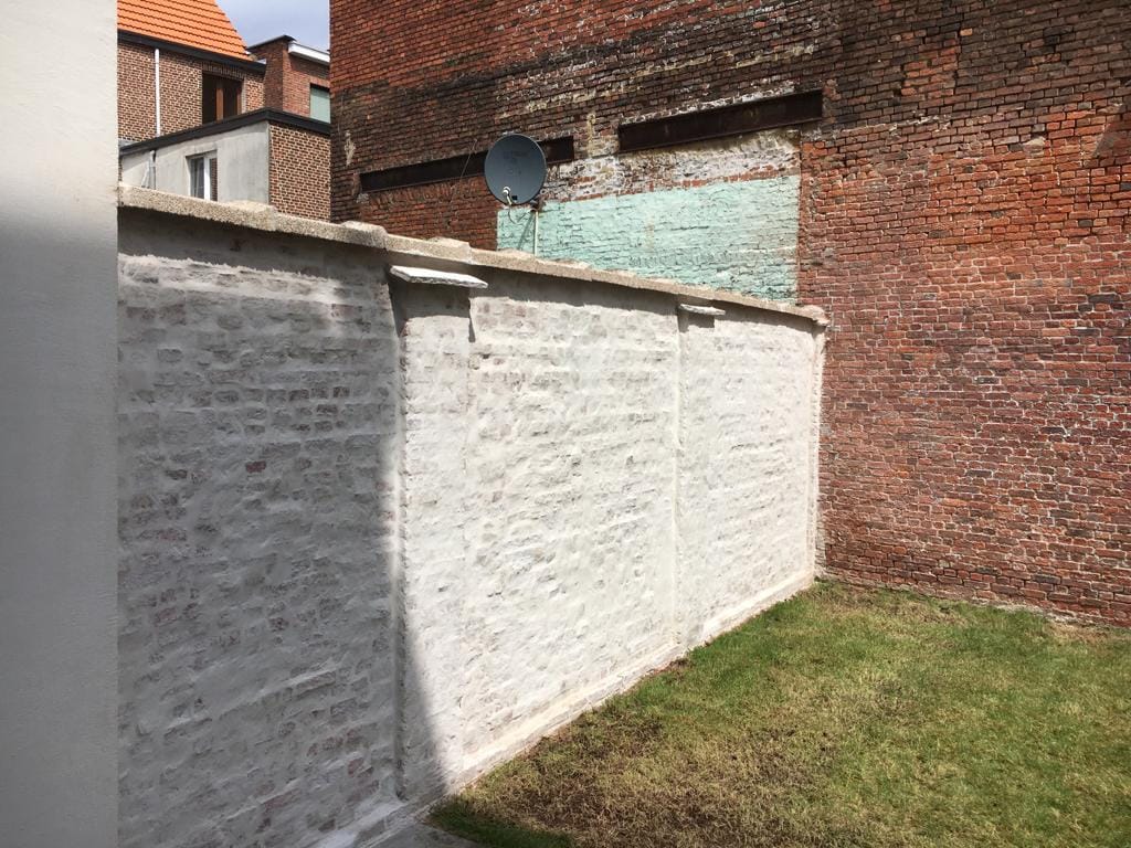 Dezelfde tuinmuur na het kaleien, egaal wit afgewerkt